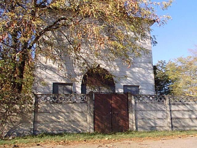 A white building with an arched entrance behind a wall and a red gate