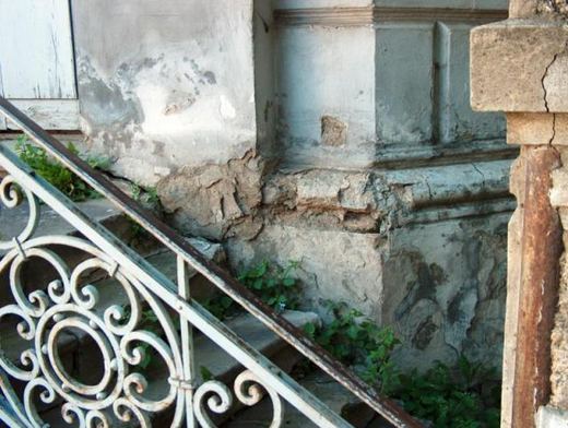 Damaged plinth beside a wrought-iron stair railing