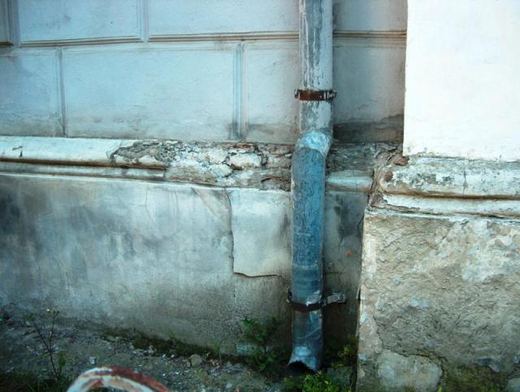 A drainpipe beside a damaged section of wall